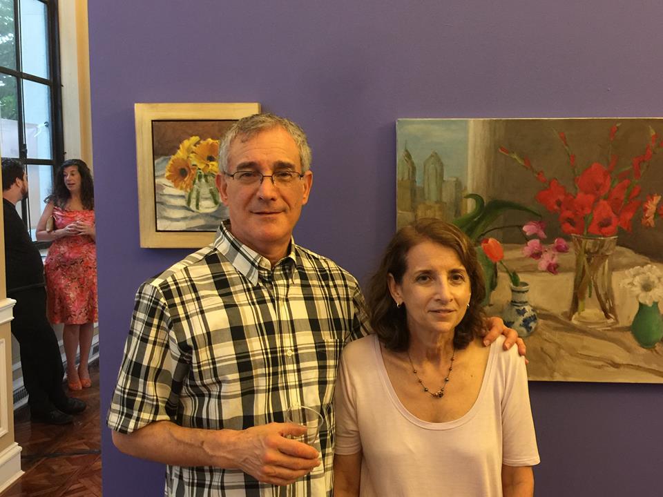 Joyce Millman (right) with husband, Gordon in front of her paintings [(left): “Tranquility,” (right): “City View”].